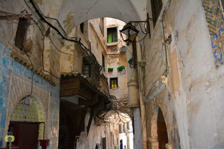 Upper floors almost meeting overhead, the alley in permanent shade.