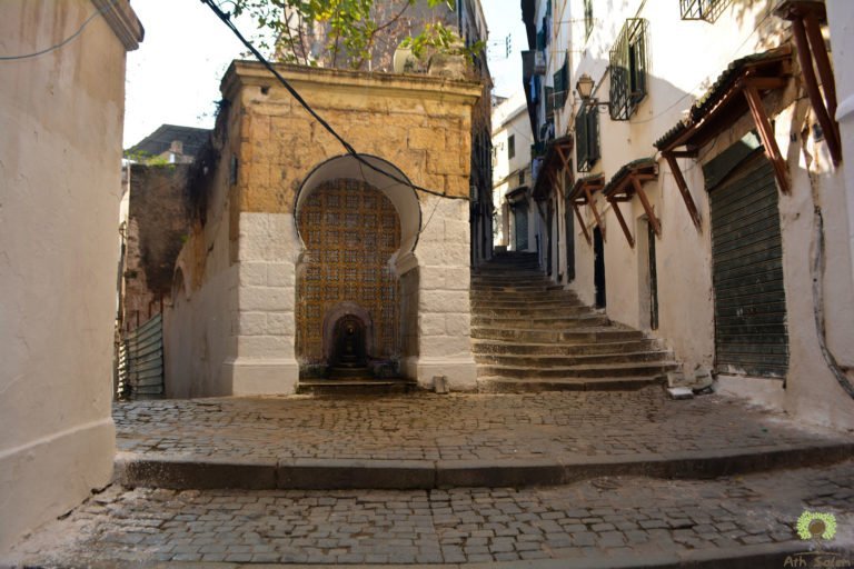 An arched fountain niche set into the wall at the foot of a stair.