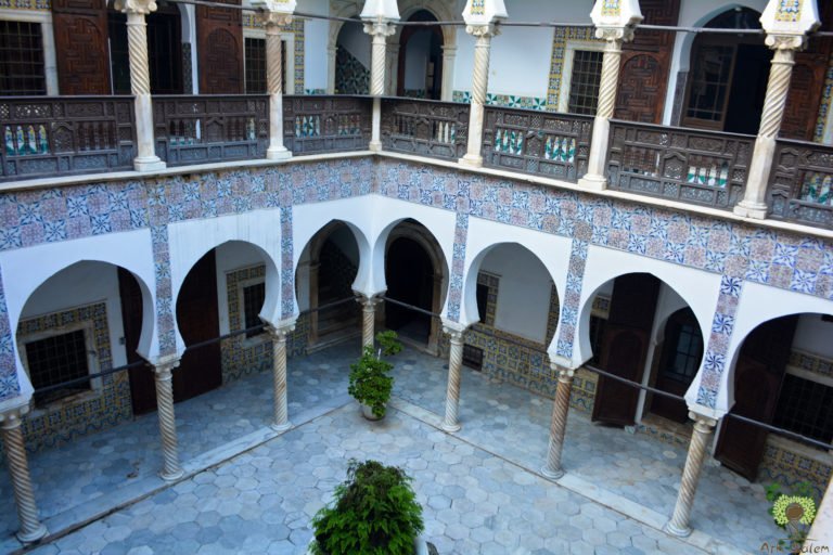 A courtyard of arcaded galleries, tiled to head height, planted at the centre.