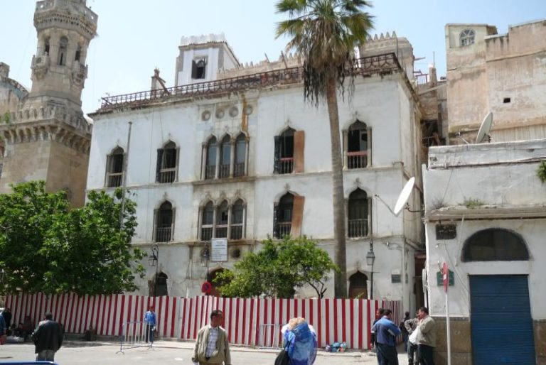 A palace front on the lower slope, palms along the street.